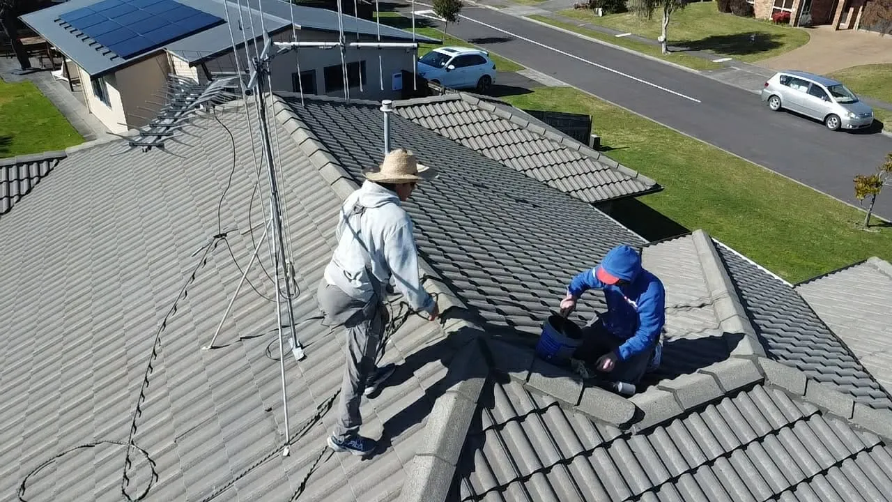 Two roofers working along the ridge line of a tile roof on a sunny day